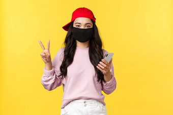 科维德社会距离生活方式防止病毒传播概念可爱的十几岁的亚洲女孩保护脸面具红色的帽会议朋友夏天周末智能手机使和平标志