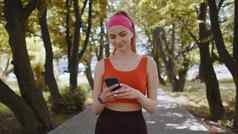 运动健身体育运动跑步者女孩走智能手机听音乐耳机公园