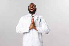 绝望的非裔美国人医生恳求乞讨神怜悯新闻手祈祷哭心关闭眼睛显示天空穿白色外套求情人保持安全科维德流感大流行