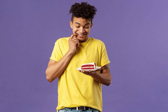 庆祝活动聚会，派对假期概念肖像的男朋友<strong>抵制</strong>诱惑吃一块蛋糕咬嘴唇微笑急切的咬甜点犹豫紫色的背景