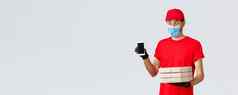 食物交付应用程序在线杂货店非接触式购物科维德概念逗乐有趣的快递红色的统一的脸面具手套显示智能手机屏幕应用程序持有披萨盒子