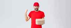 食物交付检疫保持首页订单在线概念兴奋快乐快递红色的t恤帽欢乐持有美味的披萨盒子拳头泵灰色背景