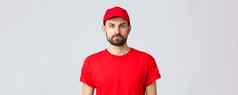 在线购物交付检疫外卖概念年轻的英俊的有胡子的快递红色的服务统一的帽t恤员工工作转让订单