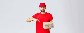 食物交付检疫保持首页订单在线概念自信友好的快递红色的统一的帽t恤员工带订单披萨指出手指盒子灰色背景