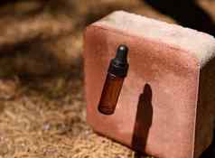 瓶化妆品石油血清铸造影子粉红色的石头背景下降干conifero针