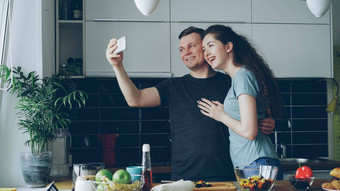年轻的快乐夫妇在线视频调用智能手机相机烹饪厨房首页
