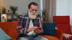 高级祖父坐着沙发智能手机分享消息社会媒体应用程序
