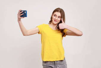 肖像乐观波浪头发的女人年轻的年龄黄色的休闲风格t恤采取自拍会说话的视频调用显示拇指