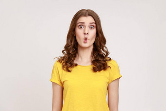 肖像迷人的有趣的青少年女孩波浪头发黄色的t恤显示鱼脸鬼脸撅嘴嘴唇使荒谬的幼稚的滑稽的鬼脸