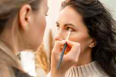 化妆艺术家使专业化妆年轻的女人工作室