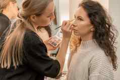 化妆艺术家使专业化妆年轻的女人工作室