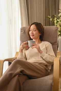 愉快的年轻的女人休息舒适的扶手椅喝热茶支出休闲周末首页