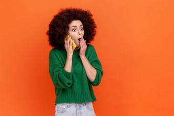 惊讶女人非洲式发型发型穿绿色休闲风格毛衣会说话的细胞电话听力令人震惊的新闻覆盖口棕榈