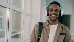 肖像年轻的英俊的学生非裔美国人种族站宽白色宽敞的走廊大学hedphones相机微笑