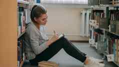 年轻的美丽的梦幻学生女孩坐着地板上轻盈图书馆书架写作作文字帖天花板
