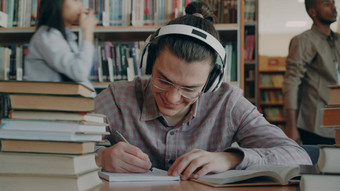 年轻的英俊的高加索人小学生坐着表格大学校图书馆写作字帖微笑积极的快乐书说谎表格