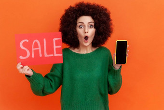 惊讶女人非洲式发型发型穿绿色休闲风格毛衣站出售卡手显示细胞电话空屏幕