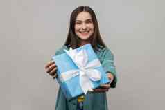 年轻的成人女持有蓝色的包装礼物盒子给现在微笑相机