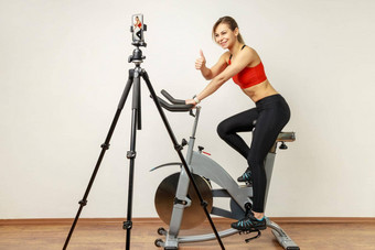 女人记录<strong>教程</strong>视频细胞电话三脚架骑锻炼自行车显示拇指