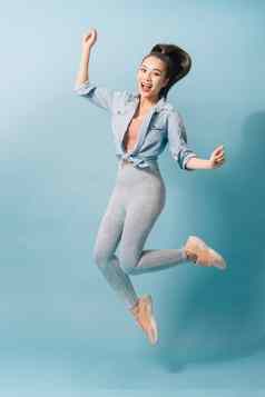 完整的长度肖像快乐的年轻的女人跳庆祝光蓝色的背景