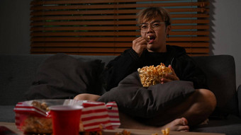 年轻的亚洲男人。看吃爆米花沙发享受休闲活动首页