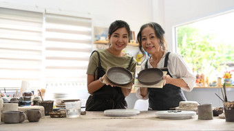 退休女人年轻的女人持有工艺品陶器微笑相机活动工艺品爱好概念