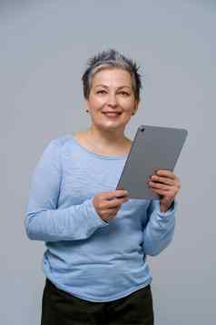 成熟的灰色头发的女人持有数字平板电脑工作购物在线检查社会媒体漂亮的女人蓝色的上衣孤立的白色背景