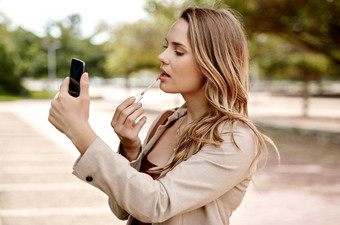 时间使移动化妆年轻的女商人应用口红智能手机城市背景