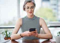 社会媒体帮助成功的成熟的女商人手机坐着桌子上