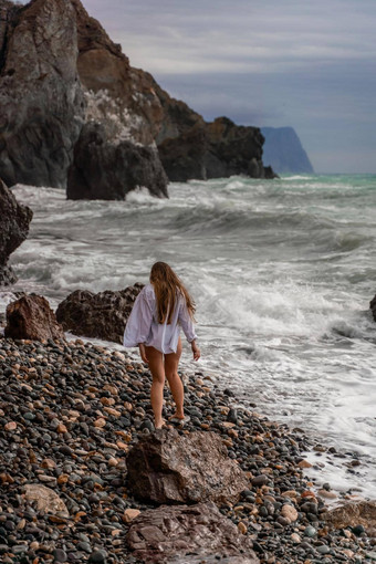 美丽的女孩白色衬衫黑色的泳衣站边缘悬崖大波白色泡沫多云的狂风暴雨的一天海云大波打岩石