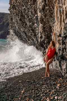 美红色的泳衣长腿提出了神奇的海滩巨大的波背景山