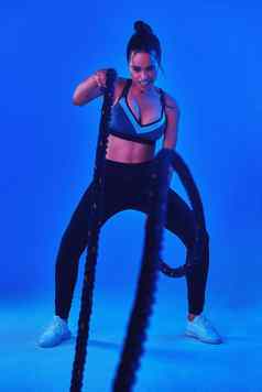 妍野兽模式完整的长度拍摄有吸引力的年轻的女运动员工作战斗绳子蓝色的背景