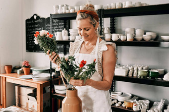 装修工作室有吸引力的成熟的女人站把花手工制作的花瓶陶器车间