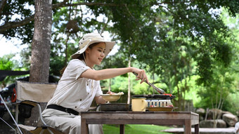 年轻的亚洲女人享受使烧烤野营河银行户外活动假期概念