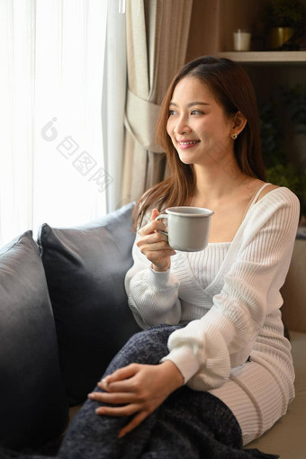 愉快的女人温暖的羊毛毛衣喝热茶休息舒适的沙发上首页
