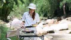 年轻的女人烧烤肉可移植的气体炉子野营自然公园美丽的一天旅行冒险假期概念