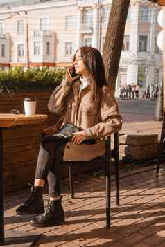 时尚的浅黑肤色的女人女人坐着表格户外咖啡馆咖啡电话女孩会说话的电话秋天走
