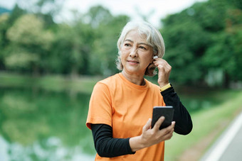 快乐运动高级女人听音乐移动电话检查智能手表公园