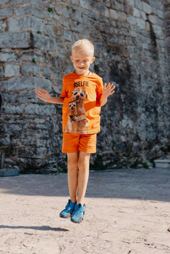 儿童户外活动微笑蹒跚学步的男孩穿橙色<strong>短裤</strong>跳运行有趣的后院阳光明媚的热夏天一天完整的长度精力充沛的男孩时尚的<strong>休闲</strong>装跳户外