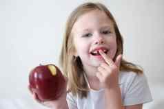 肖像微笑可爱的女孩牙齿红色的咬苹果手
