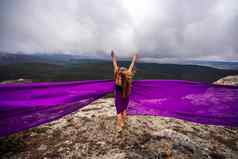 女人长头发站紫色的流动衣服流动织物山背景天空云