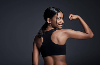 使健身日常习惯工作室肖像<strong>年轻的女运动员</strong>弯曲二头肌回来转相机灰色<strong>的</strong>背景