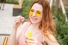 年轻的红发女人吹肥皂泡沫在户外女孩黄色的太阳镜牙套