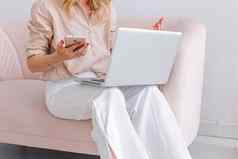 业务女人坐在灰色的开放移动PC膝盖持有粉红色的智能手机