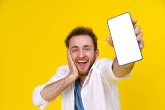 伟大的提供年轻的快乐男人。持有智能手机显示白色空屏幕令人兴奋的赢得孤立的黄色的背景庆祝成功产品放置空空间复制空间