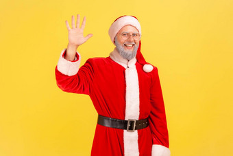积极的好上了年纪的男人。灰色的胡子穿圣诞老人老人服装挥舞着手问候相机微笑