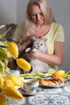 金发女郎中年拥抱小猫喝茶黄色的郁金香书