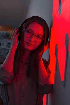 年轻的微笑女人耳机红色的霓虹灯光听音乐夜总会未来主义的霓虹灯电子声音