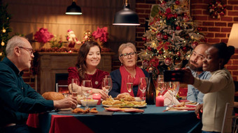 快乐的多民族家庭成员采取自拍照片智能手机坐着圣诞节晚餐表格
