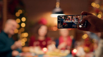节日家庭成员拍摄智能手机坐着表格享受圣诞节晚餐
